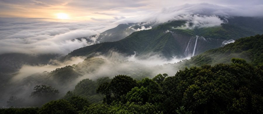 Misty Western Ghats hills with a waterfall at sunrise, representing Jungle Lodges & Resorts properties across Karnataka